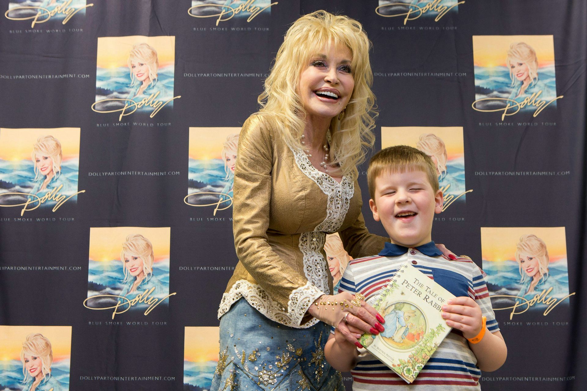 Dolly Parton presenting a book to a blind boy, with both smiling.
