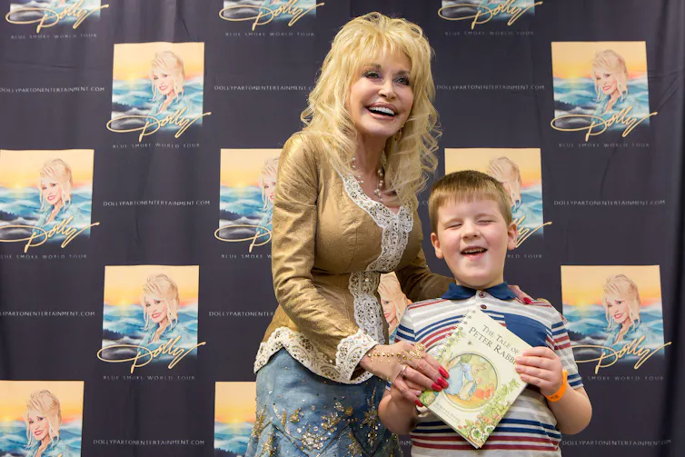 Dolly Parton presenting a book to a blind boy, with both smiling.
