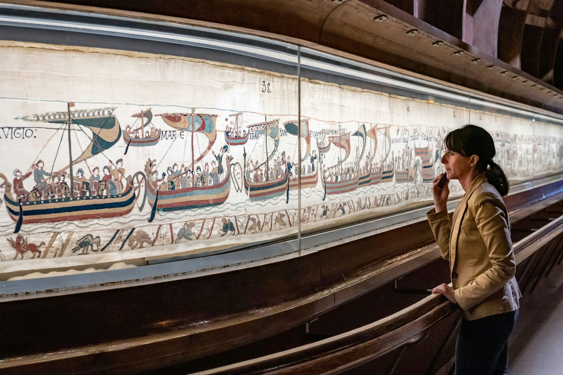 A woman viewing the Bayeux tapestry behind a curved glass case.
