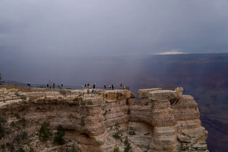 People stand on the rim of the Grand Canyon as a storm moves through.