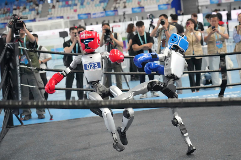 Humanoid robots compete in the free combat in the middle of a boxing ring.