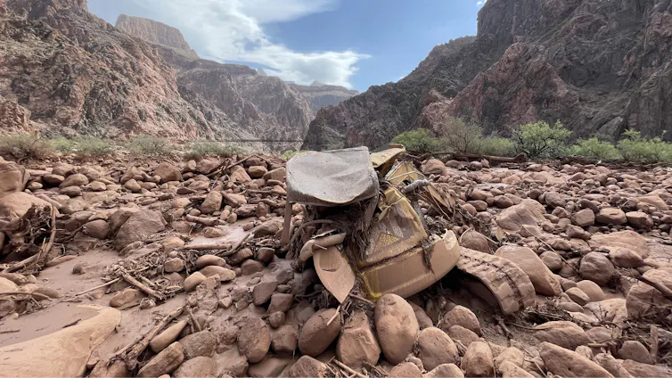 Mangled construction equipment is partially buried in boulders on the canyon floor.