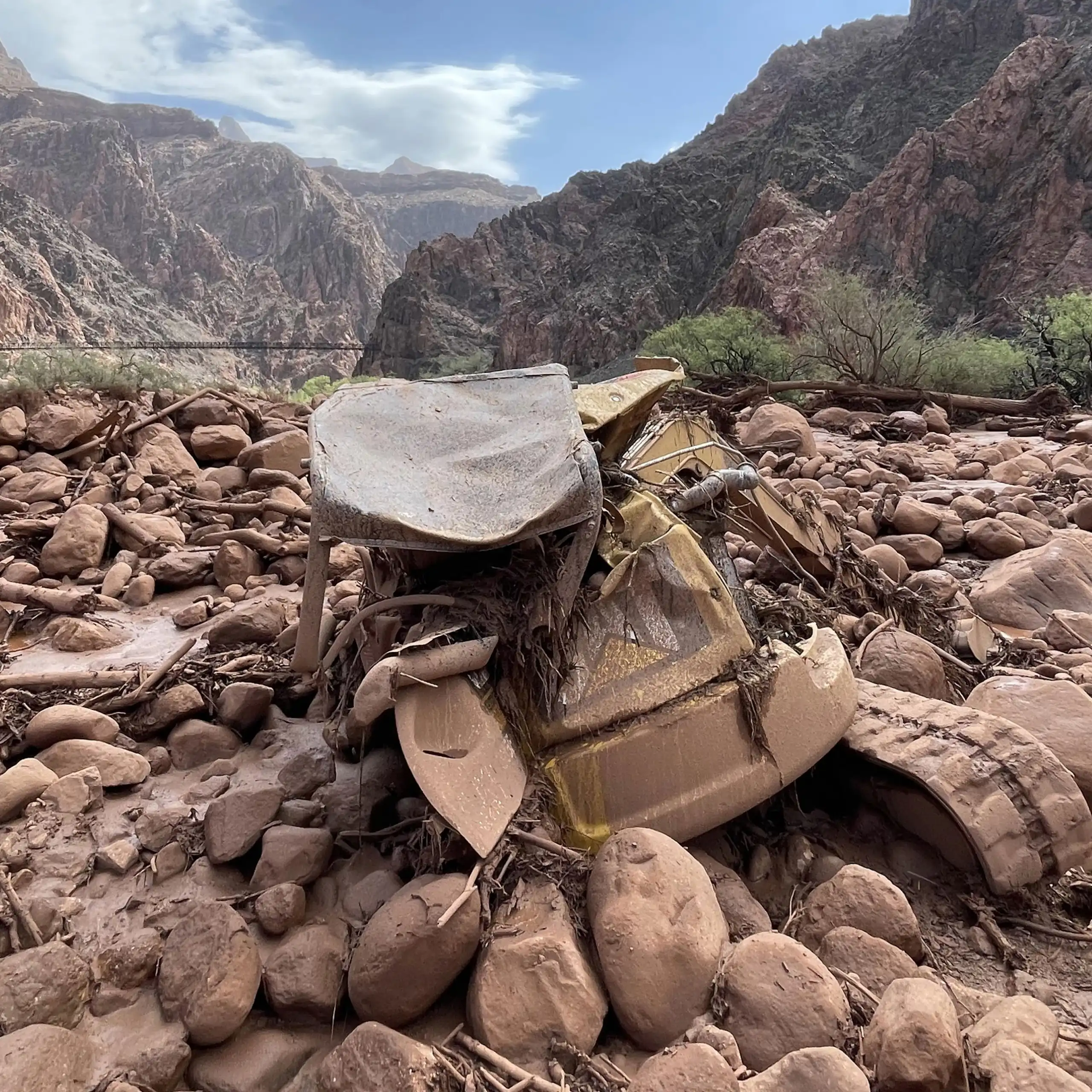 Mangled construction equipment is partially buried in boulders on the canyon floor.