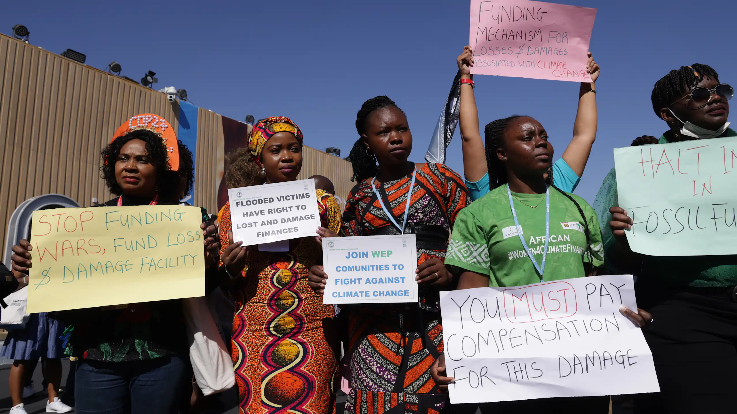 A group of people protesting with placards stating Funding Mechanism for Losses and Damages associated with climate change; Flooded victims have right to loss and damage finances and Stop Funding Wars, Fund loss and damage facility