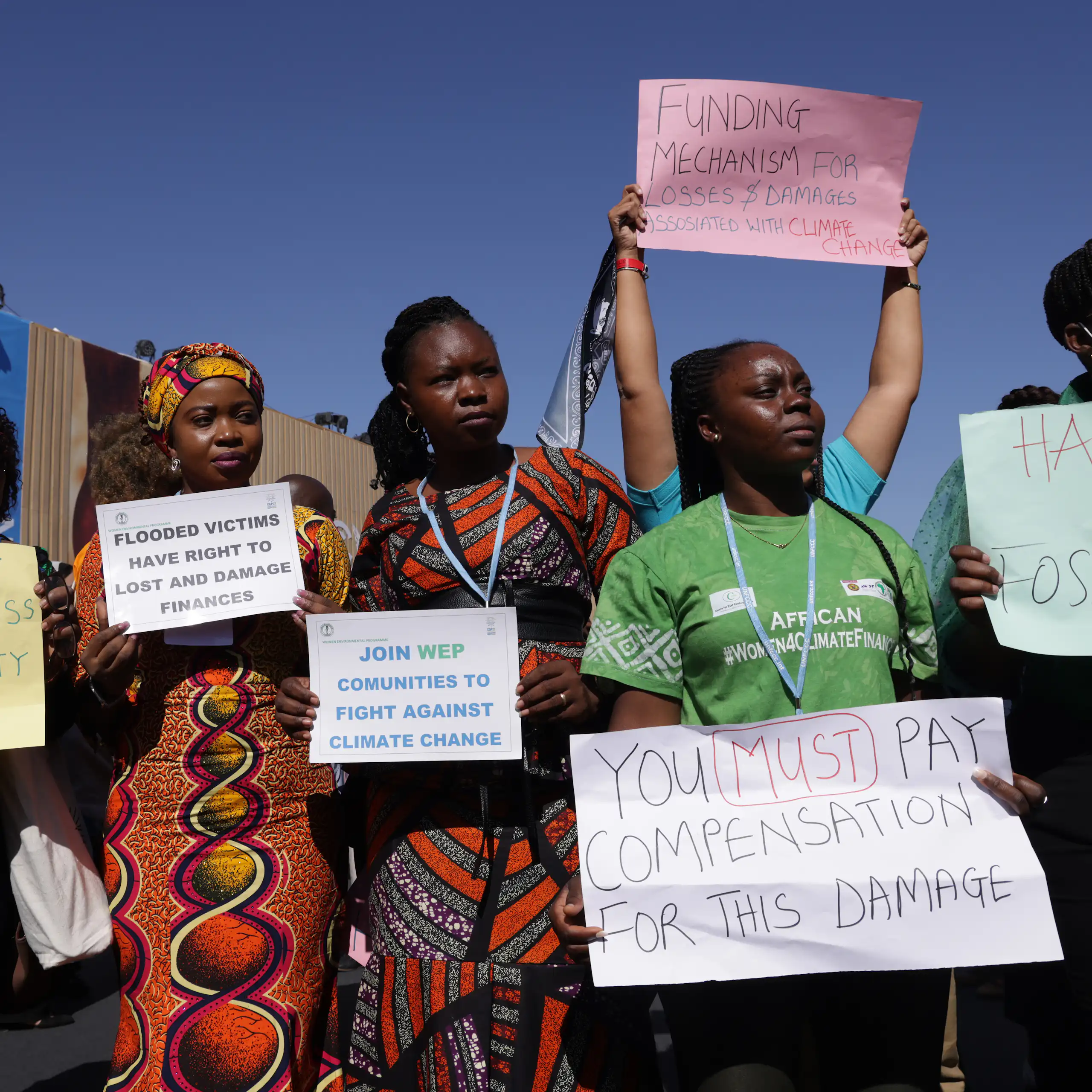 A group of people protesting with placards stating Funding Mechanism for Losses and Damages associated with climate change; Flooded victims have right to loss and damage finances and Stop Funding Wars, Fund loss and damage facility