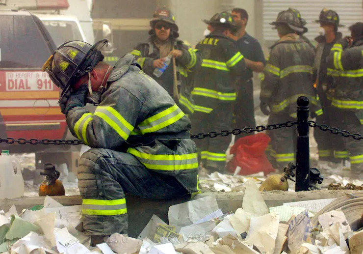 A firefighter amid papers, rubble and smoke, praying.