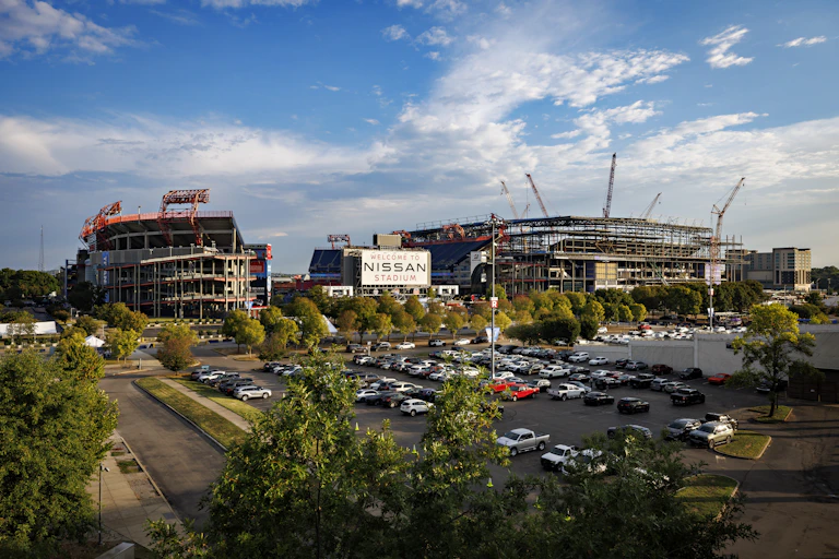 View of a parking lot in front of a large football stadium, and another stadium under construction to its right.