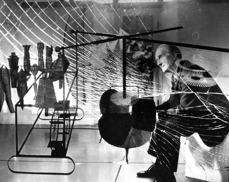 Black-and-white photo of man in suit behind large pane of shattered glass