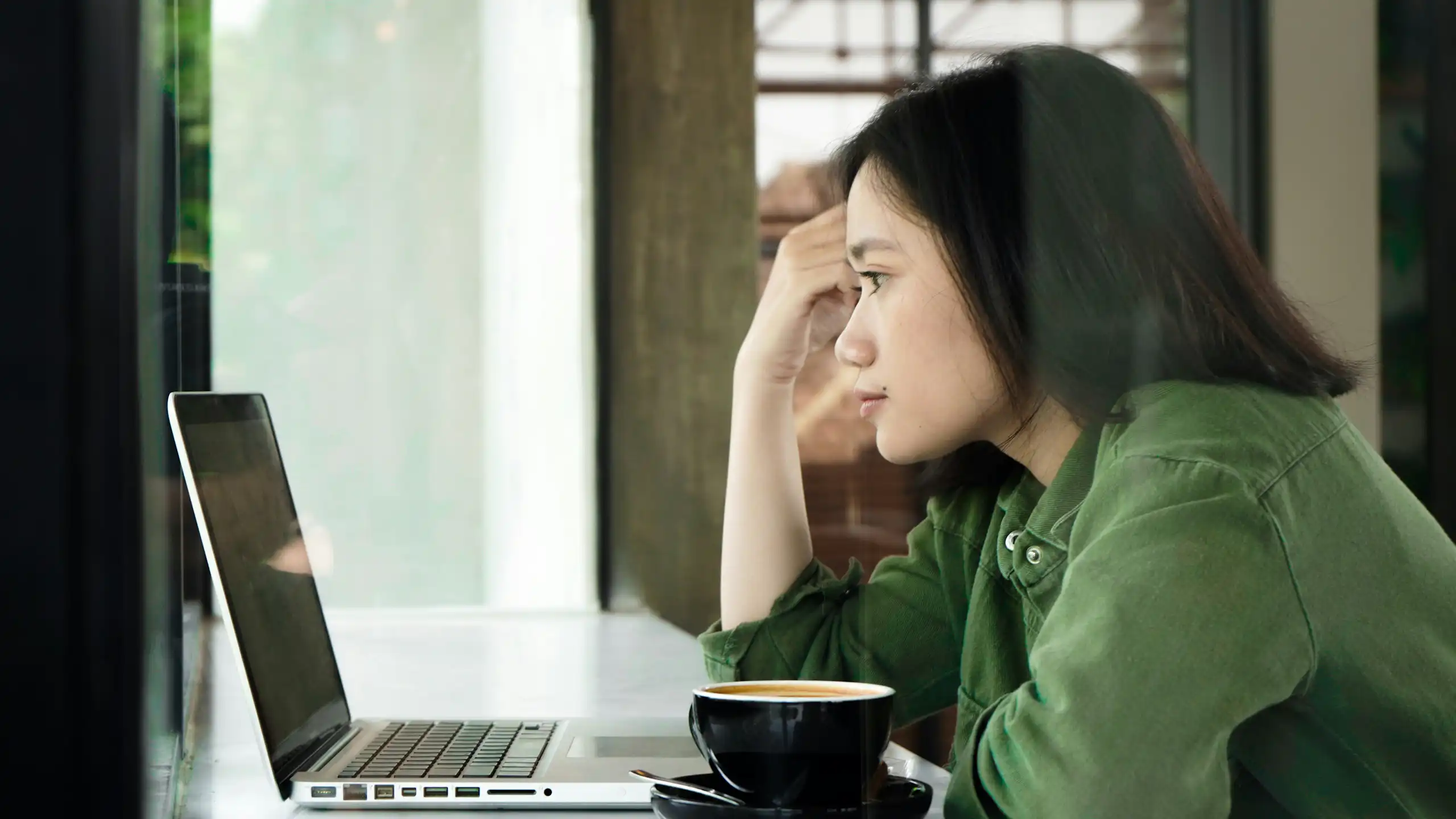 A woman in a green shirt resting her head on her hand as she looks at a laptop screen