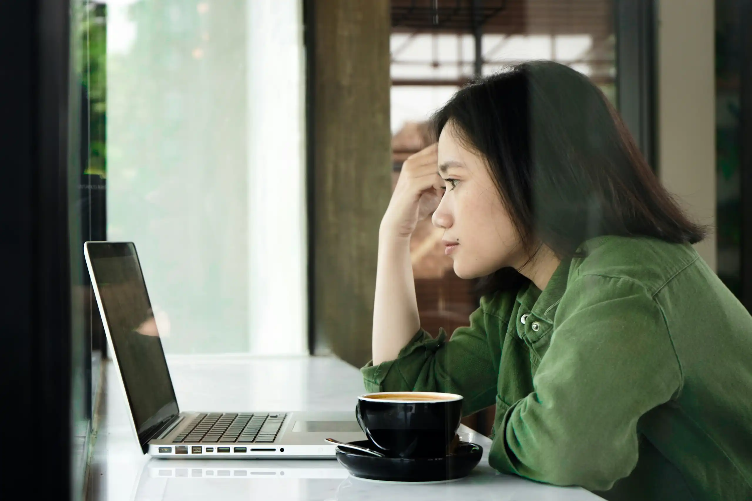 A woman in a green shirt resting her head on her hand as she looks at a laptop screen