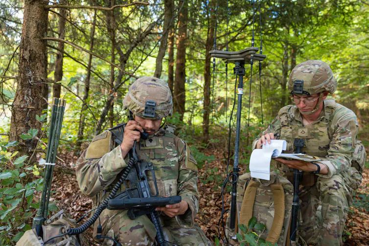 two soldiers in a forest use electronic equipment