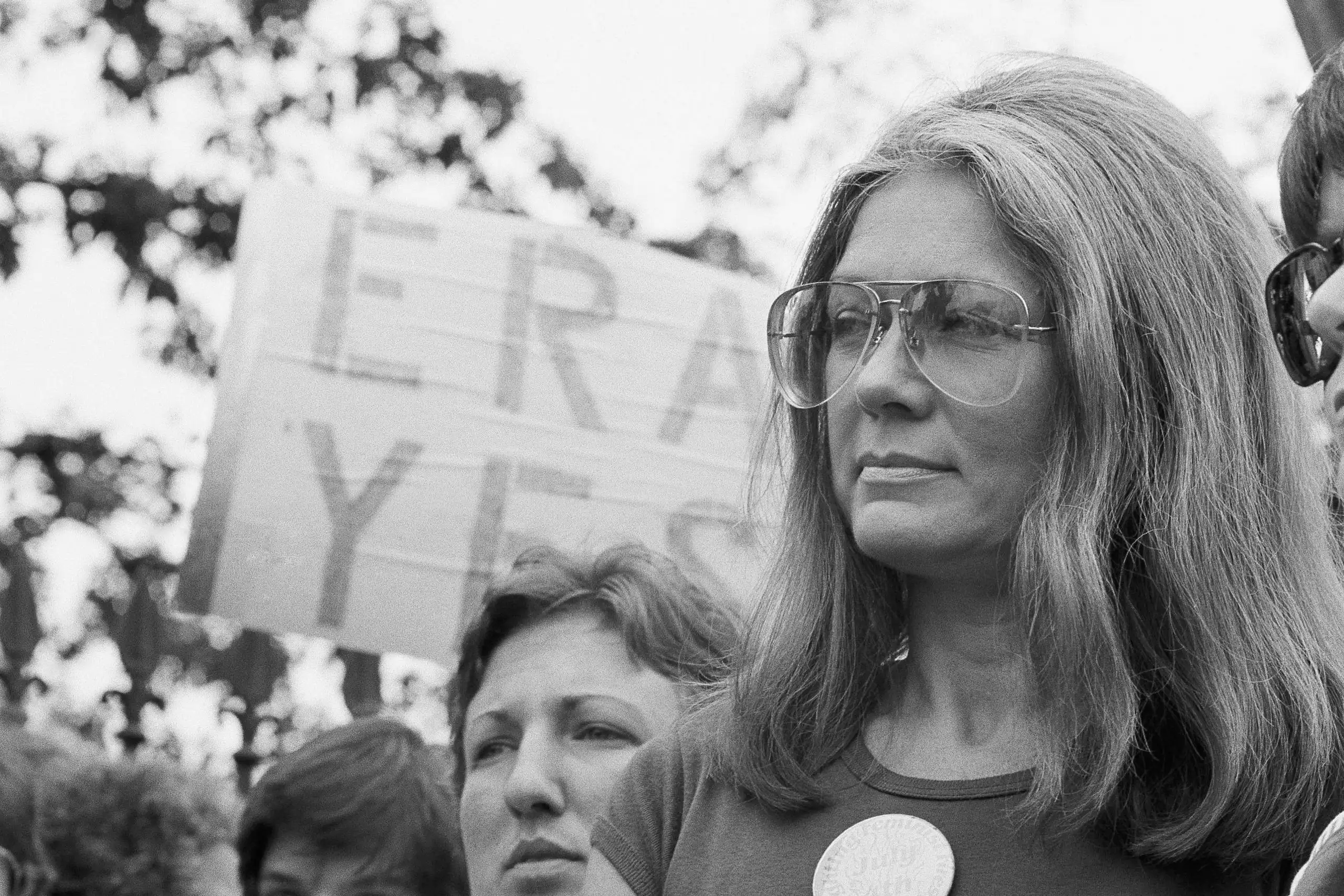 A woman in aviator sunglasses with a discerning look on her face in front of a sign that says ERA YES.