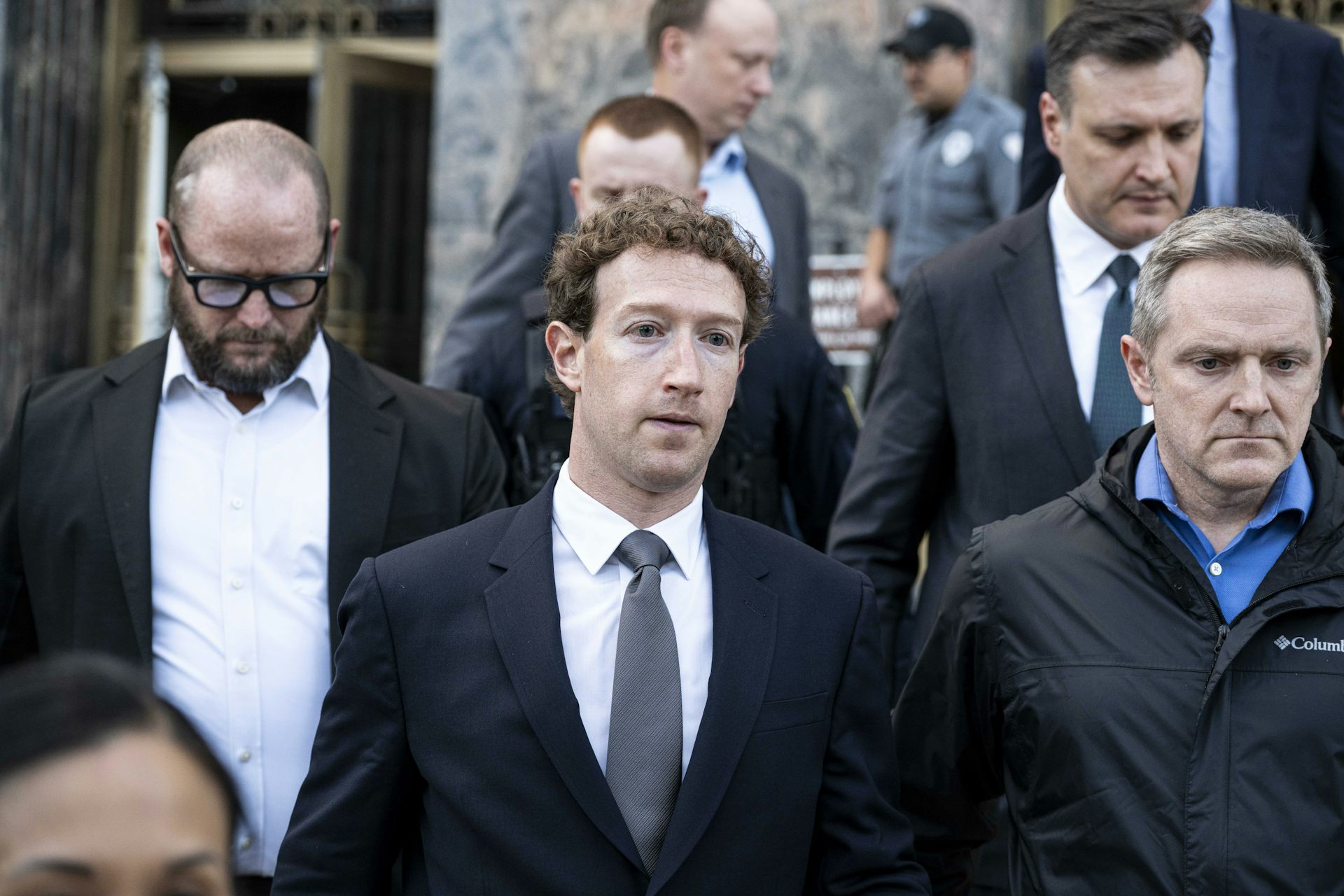 Men in suits walk outside a building.