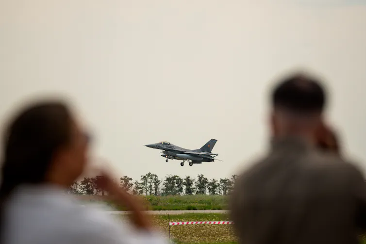 Two people watch a fighter jet take off