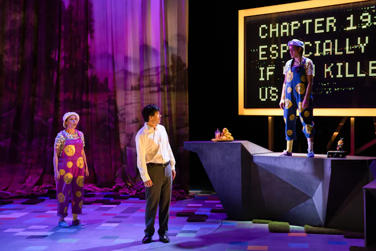 Three performers act on stage during a play.