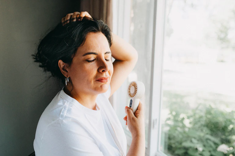 A mid-life woman cools herself with a hand-held fan