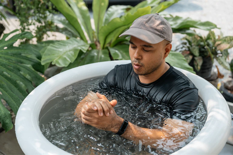 A man sitting in an ice bath checks the smartwatch on his wrist.