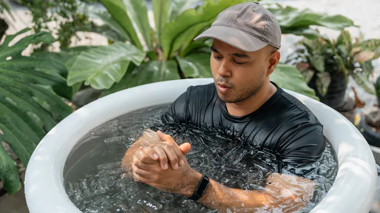 A man sitting in an ice bath checks the smartwatch on his wrist.