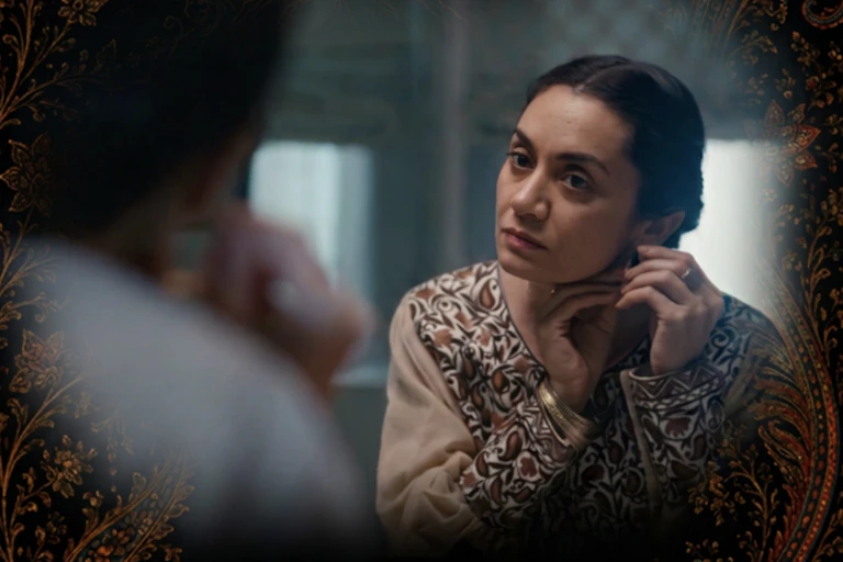 A brown woman will her hair pulled back looks into the mirror as she changes her earring.
