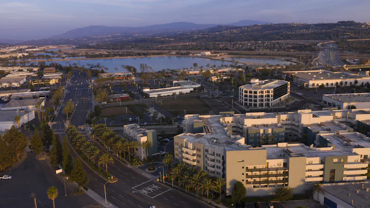 An aerial photo with palm trees, buildings, water and mountains at sunset.