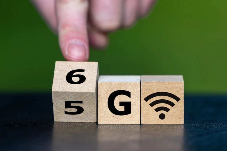 Des cubes alignés présentent des symboles écrivant "5G", mais un doigt fait tourner l'un des cubes pour écrire "6G".