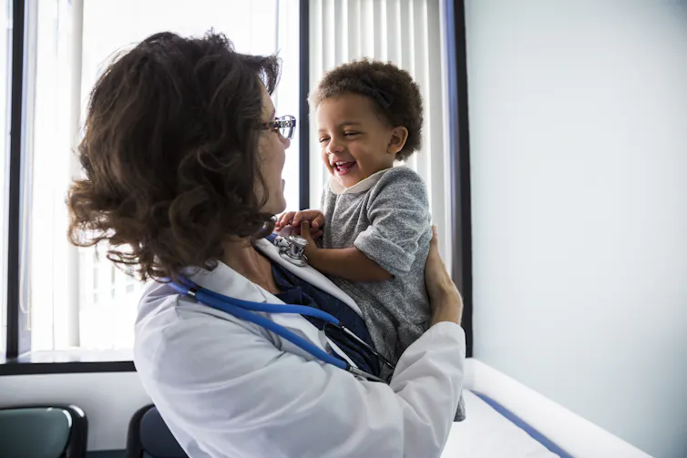 A woman doctor holds a cheerful baby girl in a medical exam room.