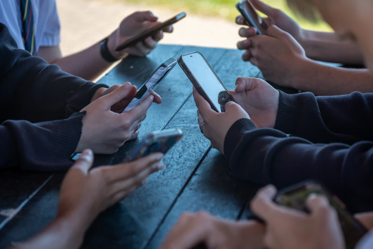 Teens look at their phones around a table.