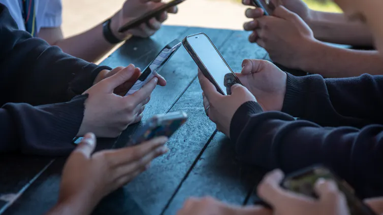 Teens look at their phones around a table.