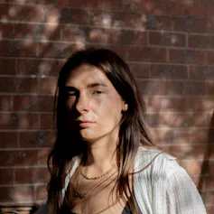 A young woman looking serious, in front of a brick wall.
