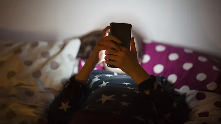 A young person lying in bed at night using a mobile phone.