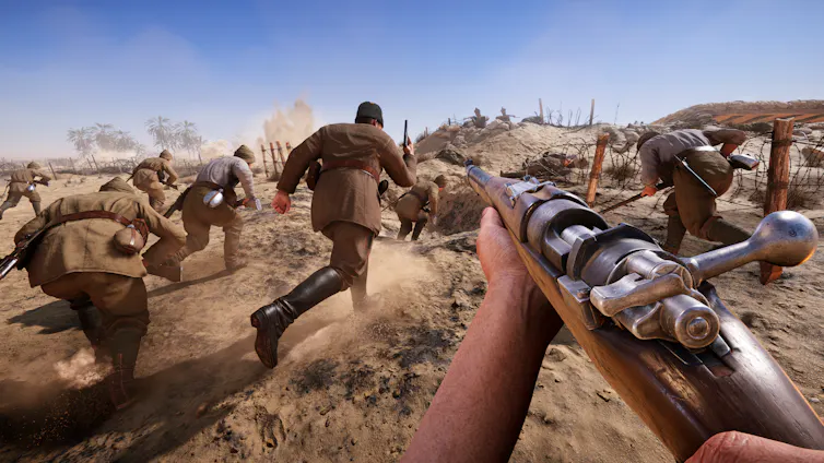 First-person view of a soldier holding a rifle while other soldiers run across a dusty battlefield towards fortified trenches and barbed wire.
