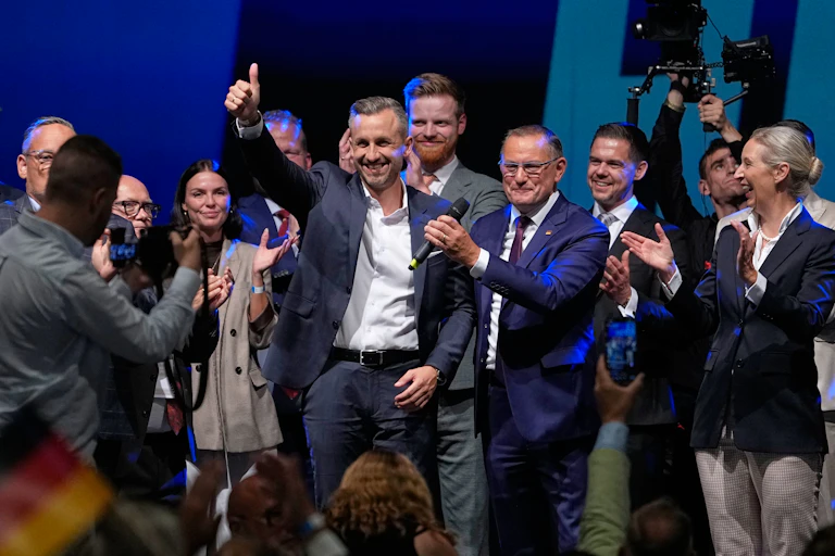 Man in suit gives a thumbs-up sign surrounded by colleagues