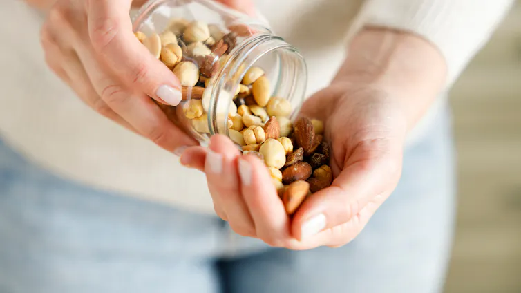 A person pours a jarful of nuts into the palm of their hand.