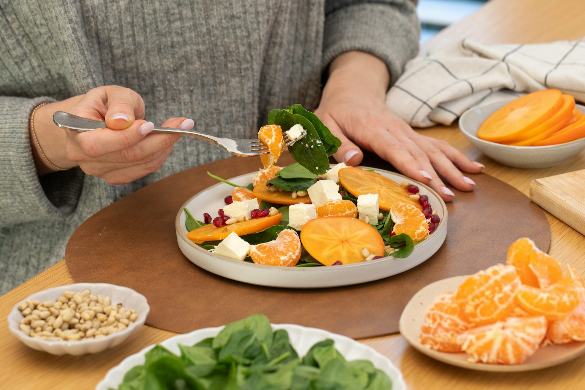 A person eats a healthy salad made with spinach, nuts, slices of orange and cheese.