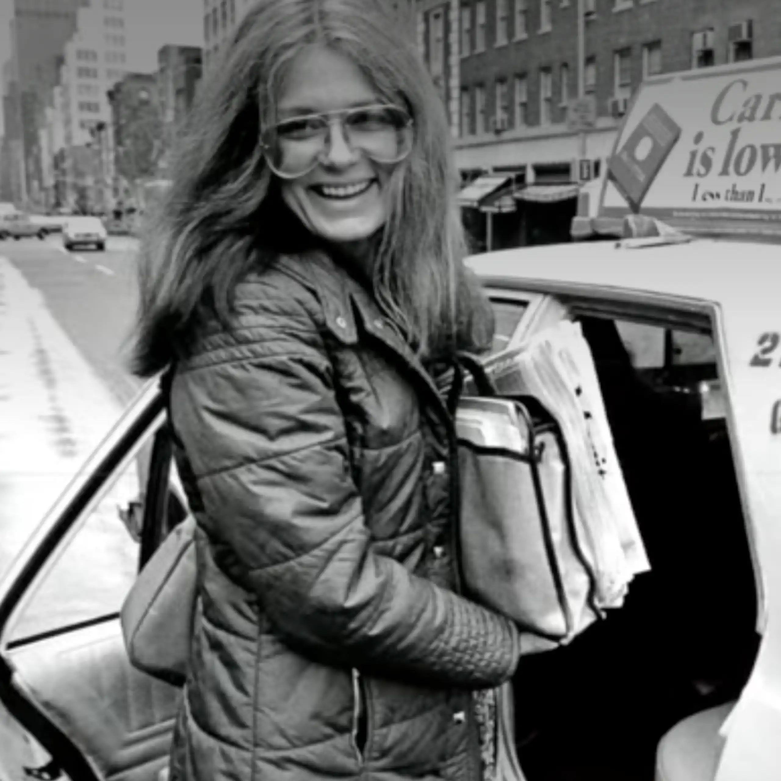 Gloria Steinem, dans les années 1970, souriante, les bras chargés, sur le point de monter dans un taxi.
