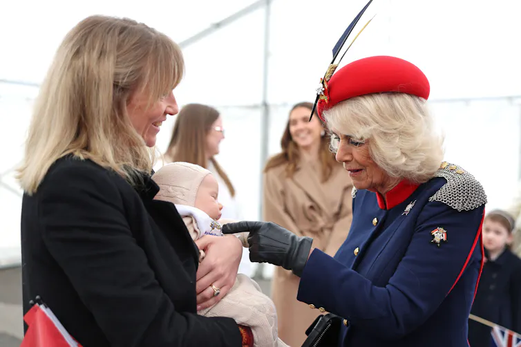 Queen Camilla pokes finger at baby held by smiling woman