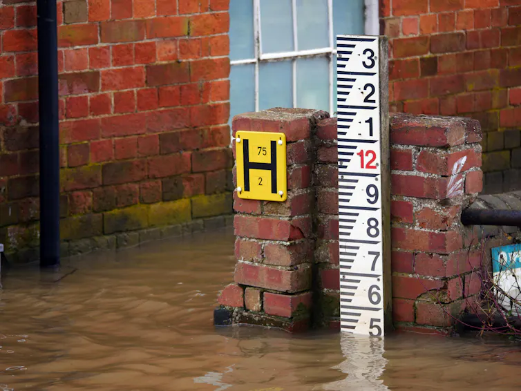 flood height marker rule in white next to brick wall of house