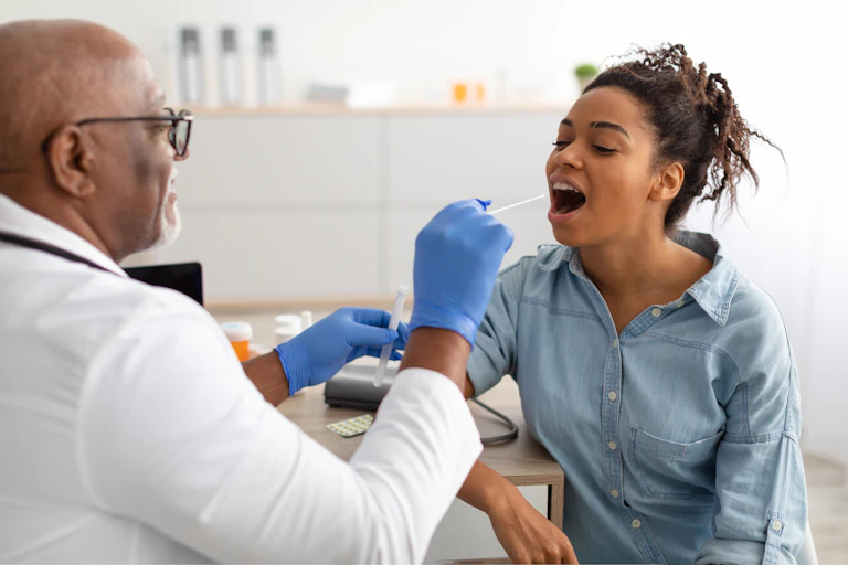 A doctor wearing gloves prepares to take an oral swab from a seated patient