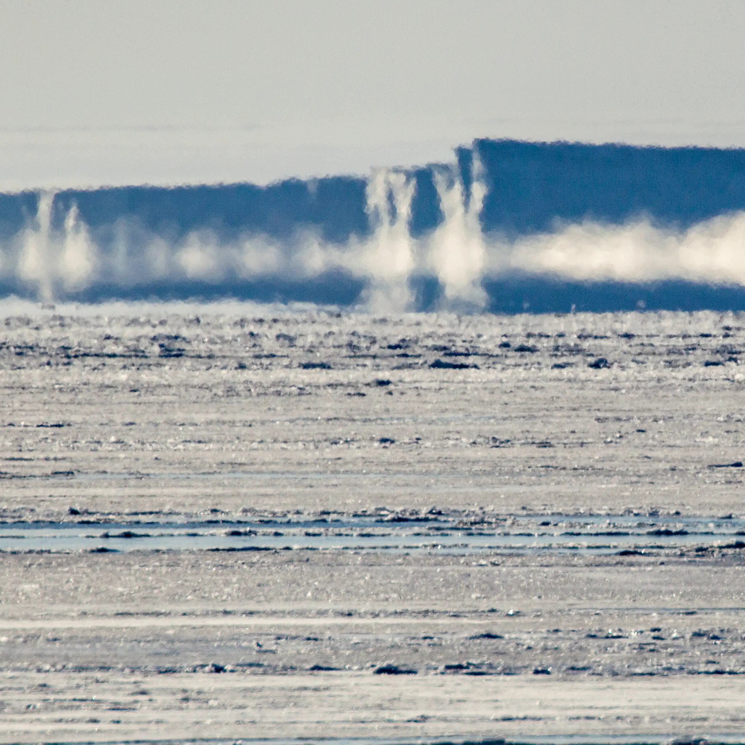 Antarctic landscape with thin sea ice and ocean patches in the foreground and misty ice cliffs in the background
