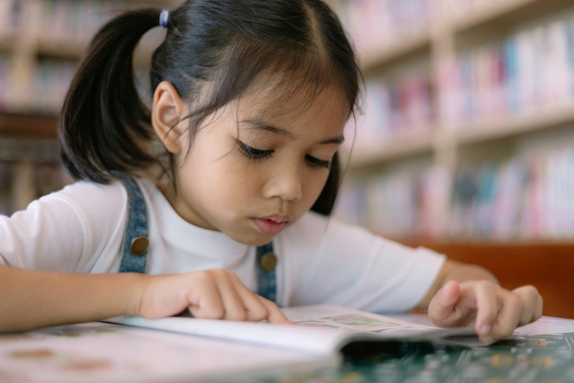 Une petite fille se concentre sur un livre dans une bibliothèque.