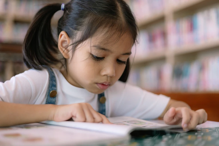 Une petite fille se concentre sur un livre dans une bibliothèque.