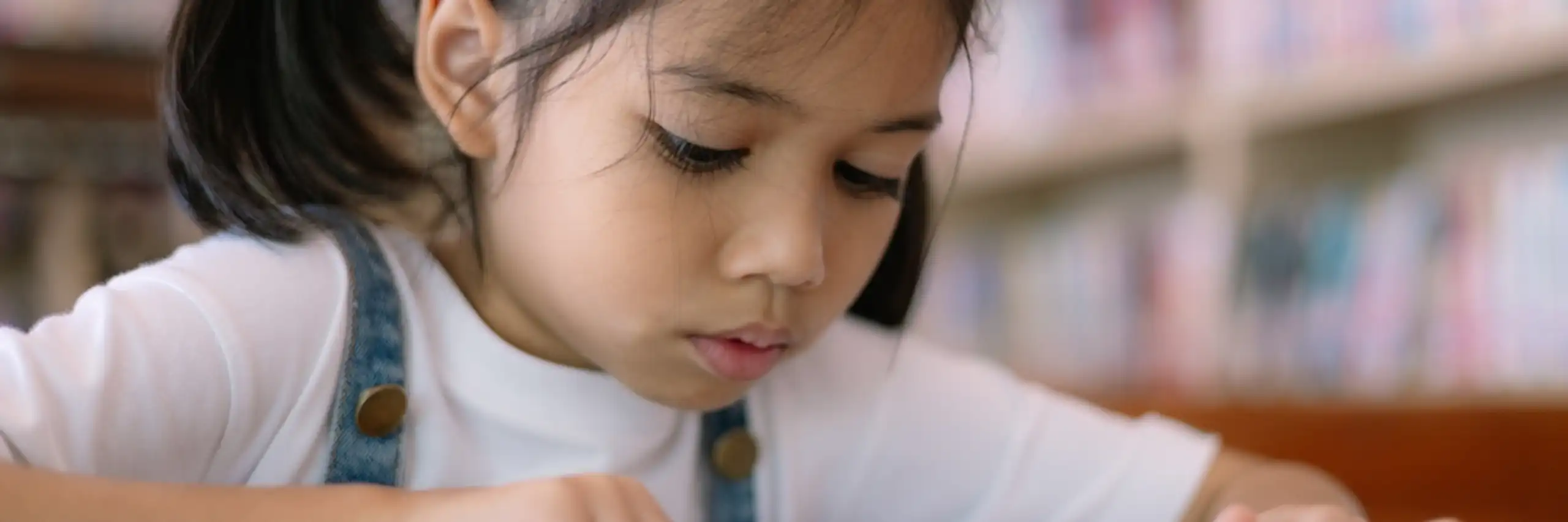 Une petite fille se concentre sur un livre dans une bibliothèque.
