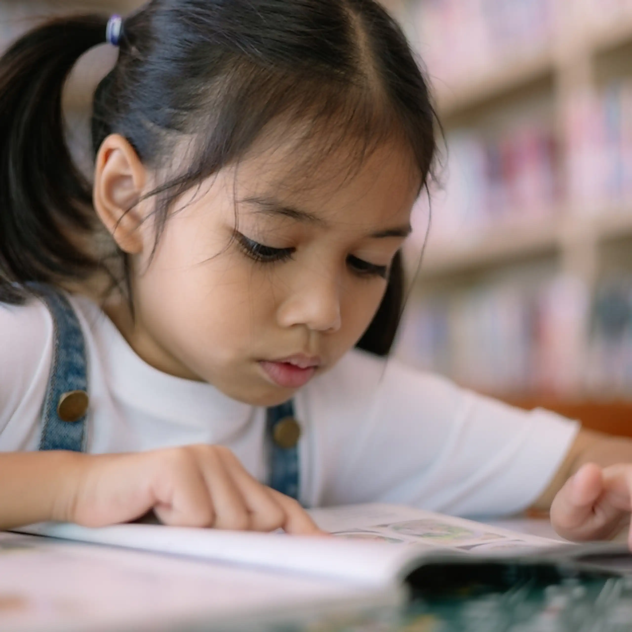 Une petite fille se concentre sur un livre dans une bibliothèque.