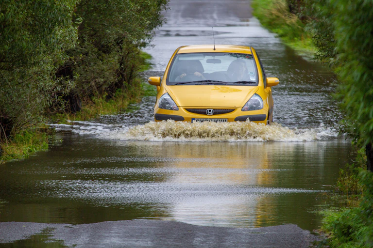 small yellow car drives through flooded country lane