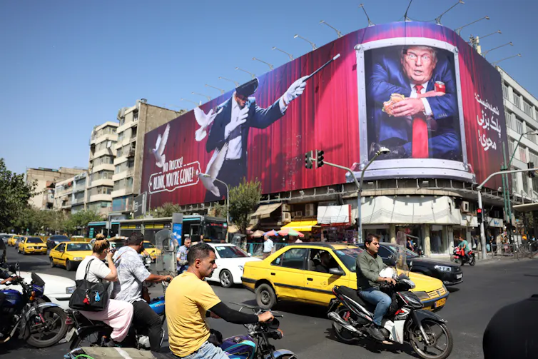 People drives cars and motorcycles in the centre of Iran past an anti-Trump banner.