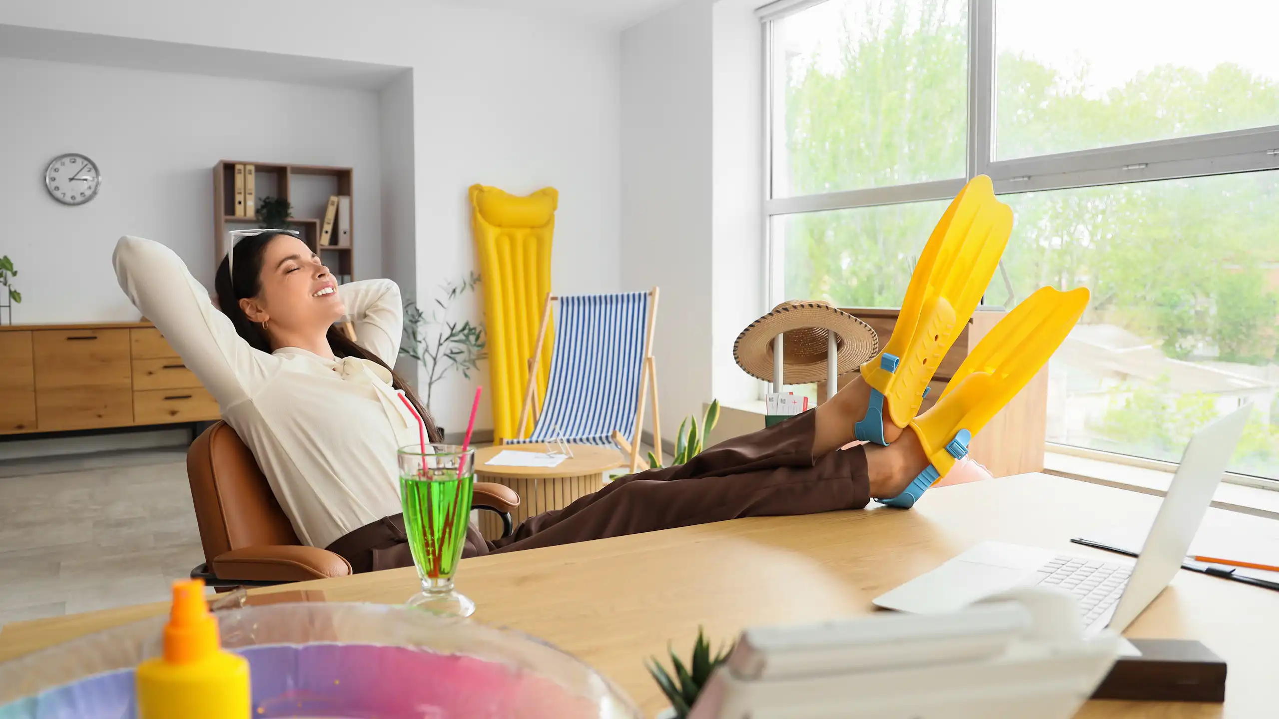 Jeune femme au bureau, les pieds chaussés de palmes posés sur sa table de travail.