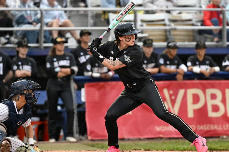 Young woman wearing black uniform anticipates a pitch while holding a baseball bat.