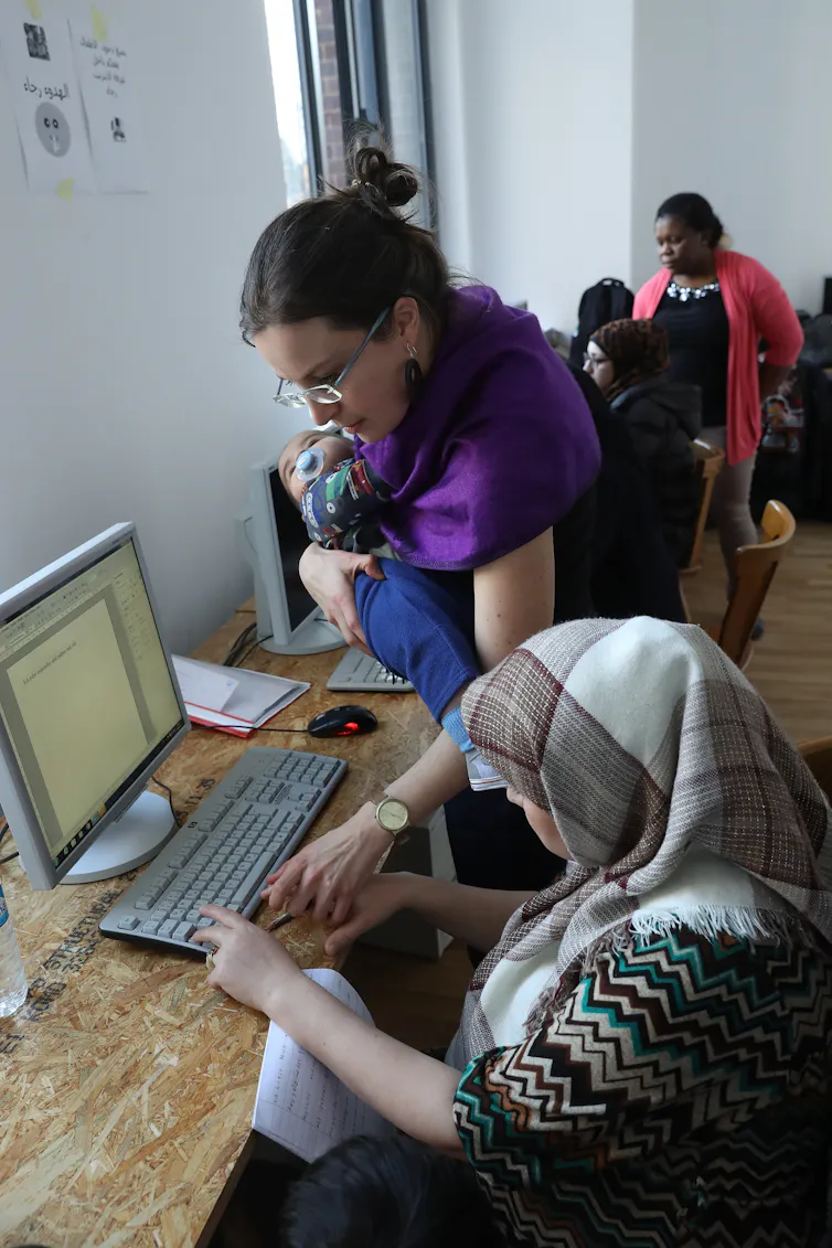 A women is teaching another woman sitting at a screen how to use the internet.