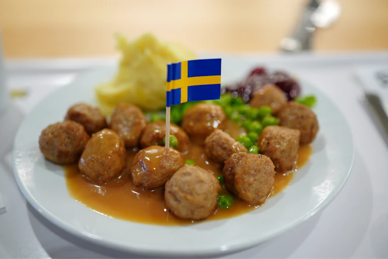A plate of IKEA meatballs, mash potato, lingonberry sauce, peas and gravy adorned with a Swedish flag