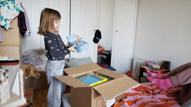 Little girl unpacking in bedroom of the new home, taking toys from cardboard box.